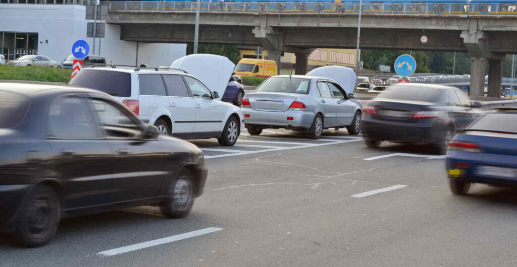 Car accident on a busy road with multiple vehicles, one having its hood open, possibly from lane splitting.