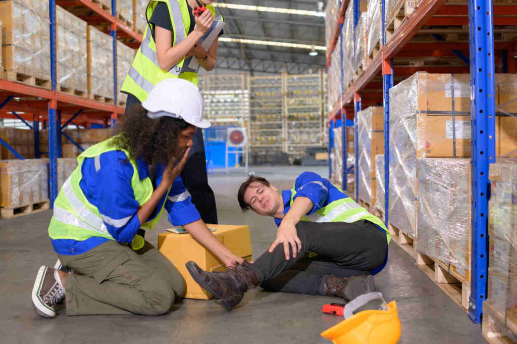 Warehouse worker injured on the job in NH, with colleagues assisting, illustrating a scenario for workers' compensation or personal injury claims.
