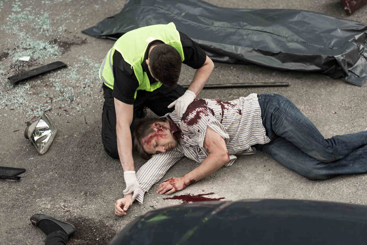 A paramedic tends to an injured person at the scene of a serious accident.